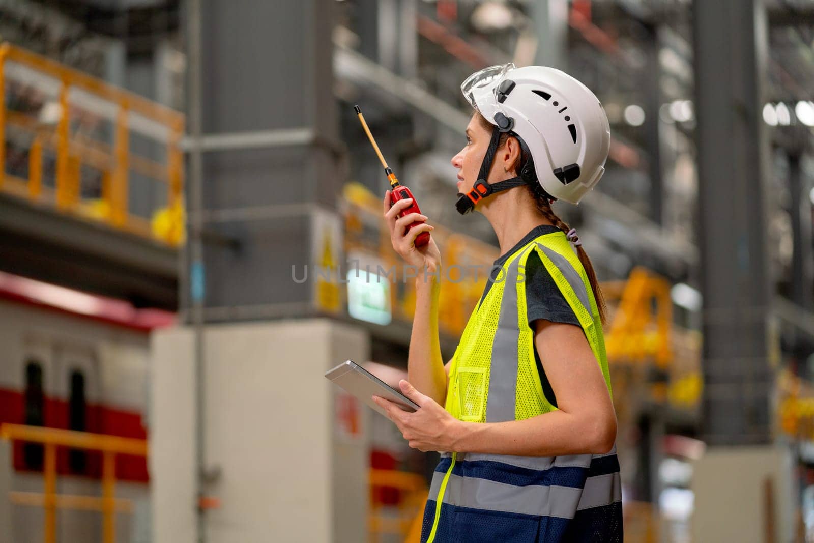 Pretty factory worker woman use walkie talkie to contact with team or co-worker and also hold tablet in concept of happiness and good system to work in workplace of industrial center.