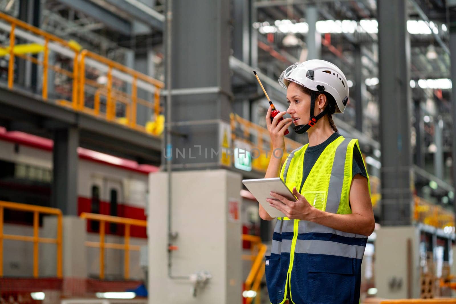 Professional engineer or technician worker woman hold tablet and use walkie talkie to communicate with other co-worker of team staffs and stay in factory industry workplace area.