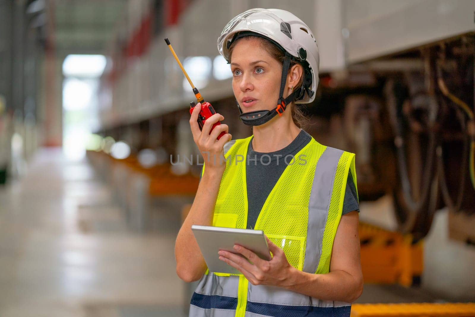 Close up professional engineer or technician worker woman hold tablet and use walkie talkie to communicate with other co-worker of team staffs and stay in factory industry workplace area.