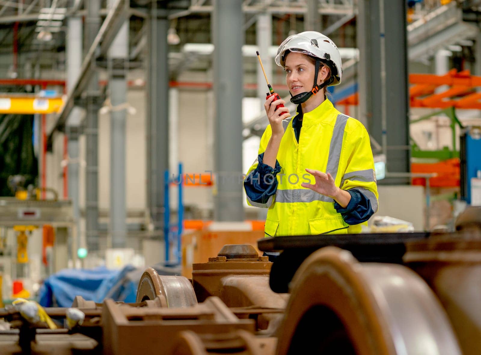 Profession engineer or technician worker use walkie talkie to contact with co-worker or team staff and stand behind part of electric train in maintenance center. by nrradmin