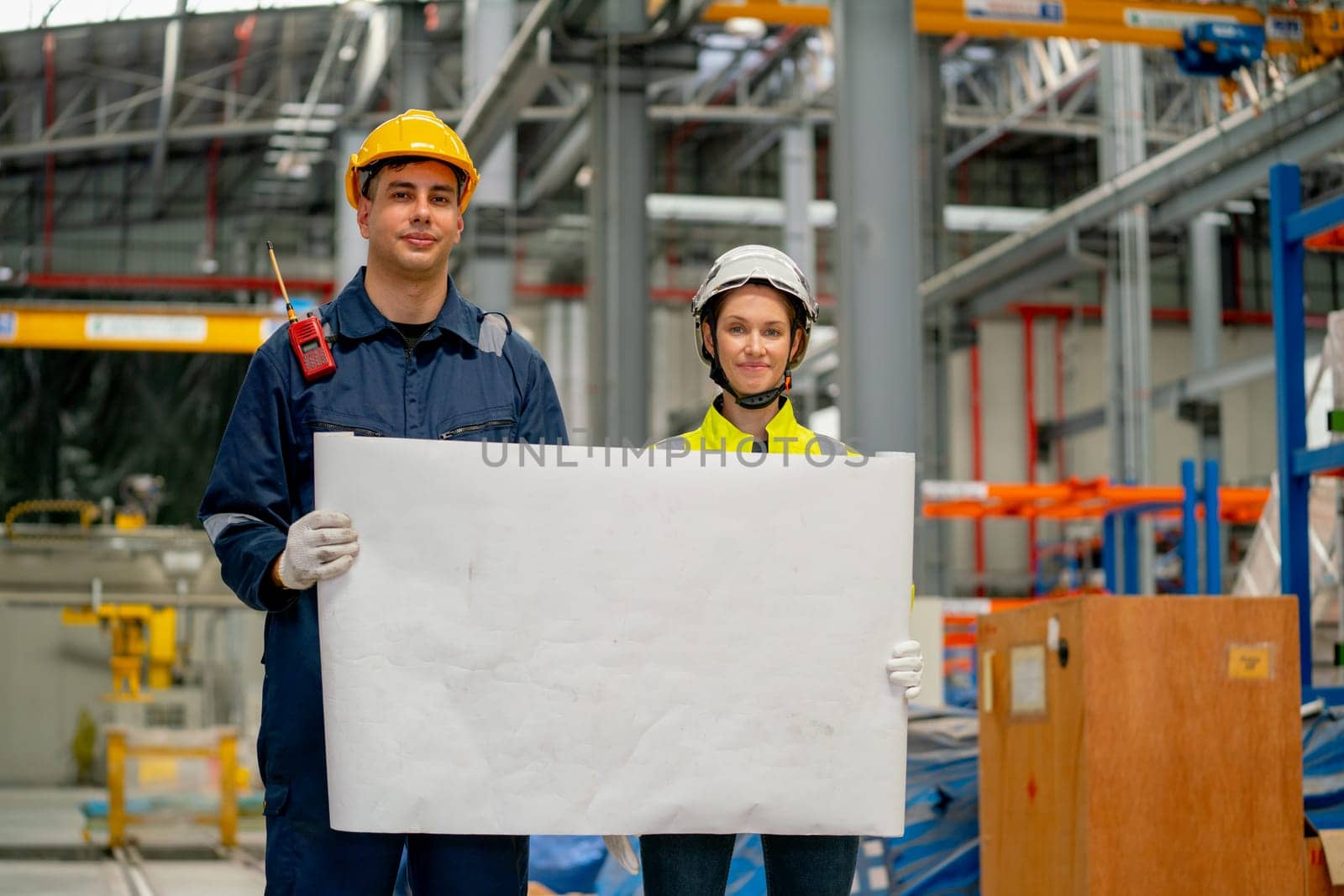 Professional engineer or technician workers man and woman hold white drawing paper and look at camera also stay in factory workplace.