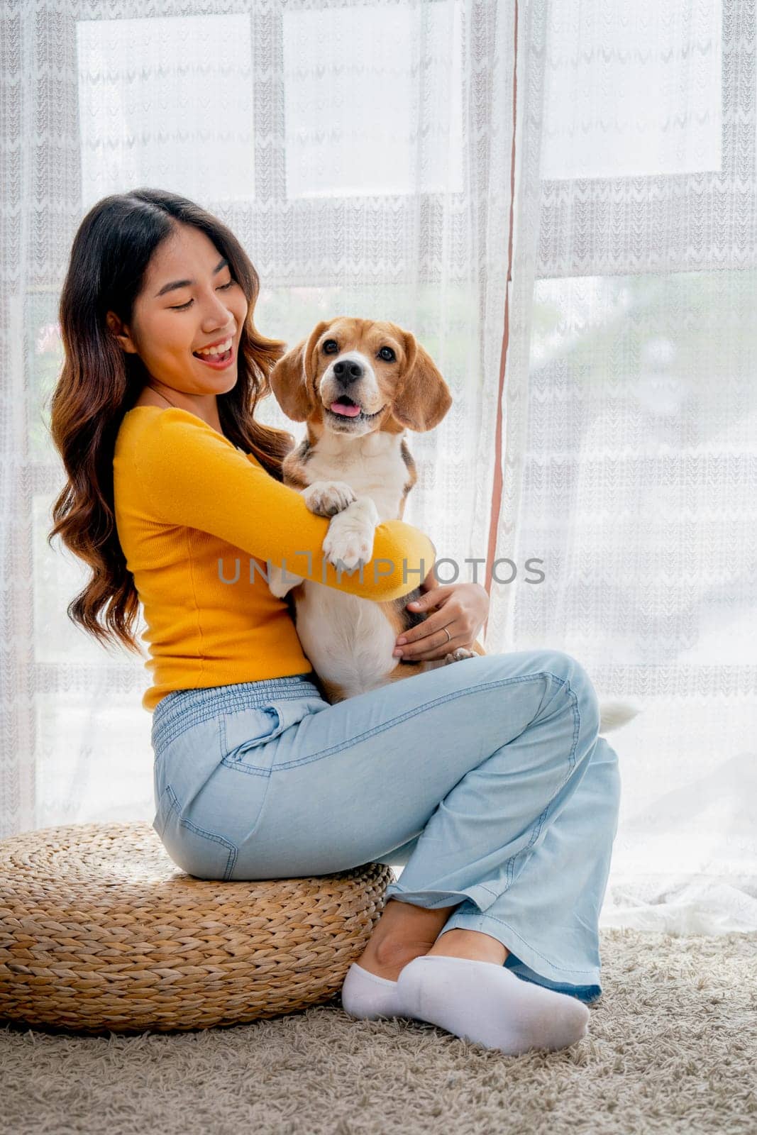 Vertical image young girl hold beagle dog and sit in front of glass door in her house and she look happy to play fun together. by nrradmin