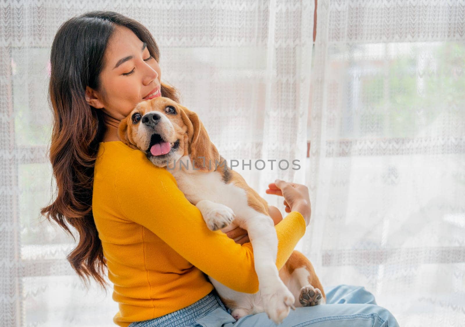 Close up young Asian girl hold and hug beagle dog and sit in front of glass door in her house and she look happy to play fun together. by nrradmin