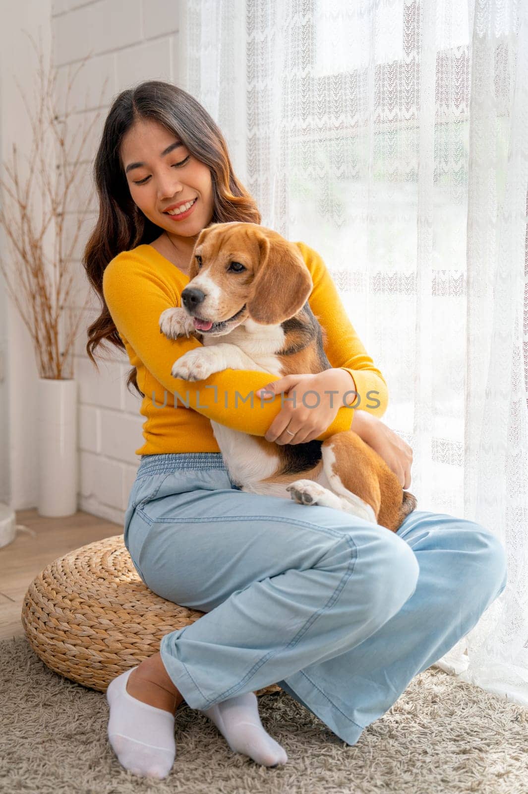 Vertical image of young Asian girl hold and hug beagle dog and sit in front of glass door in her house and she look happy to play fun together. by nrradmin