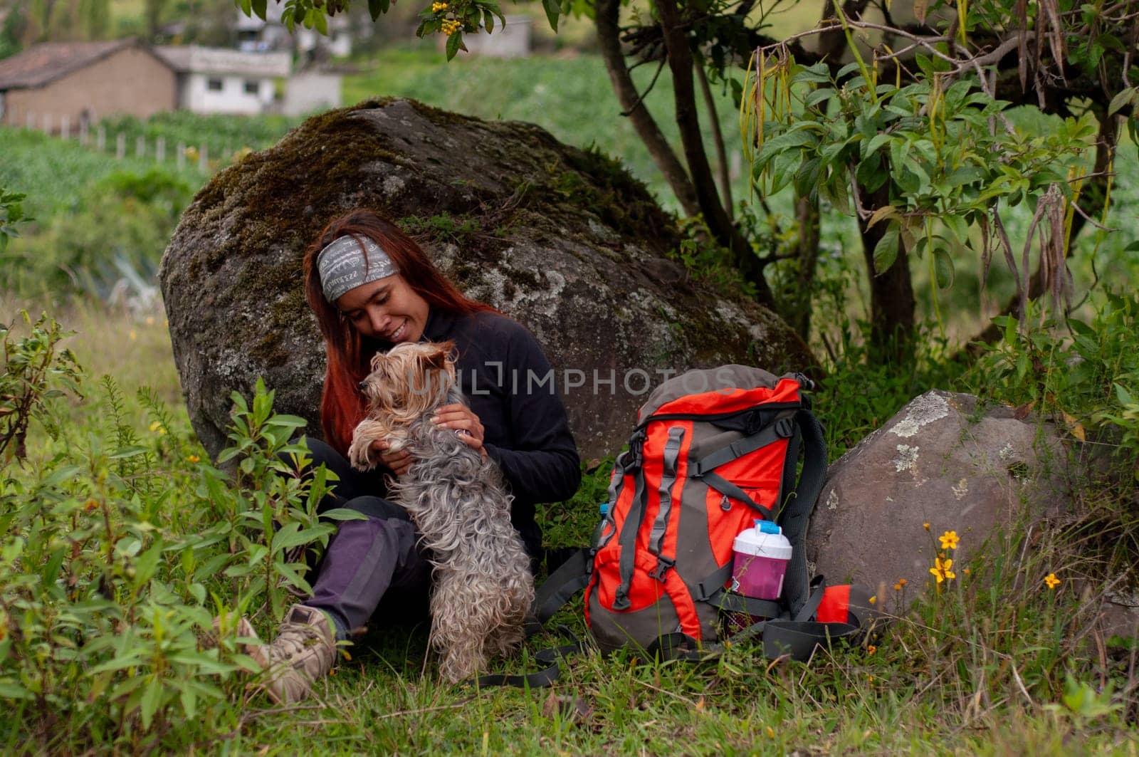 trekking lover girl resting leaning on a rock playing with her dog next to her backpack. by Raulmartin