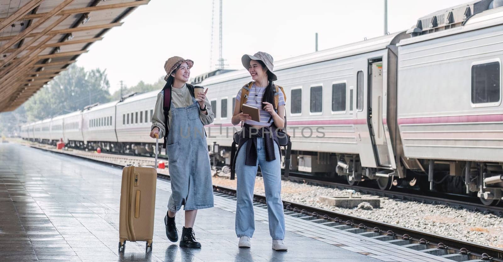 Two Asian female tourist friends are at the train station. Waiting for the train to travel to the provinces together on the weekend..