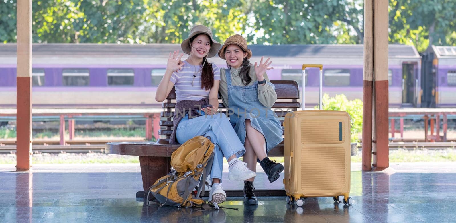 Two Asian female tourist friends are at the train station. Waiting for the train to travel to the provinces together on the weekend. by wichayada