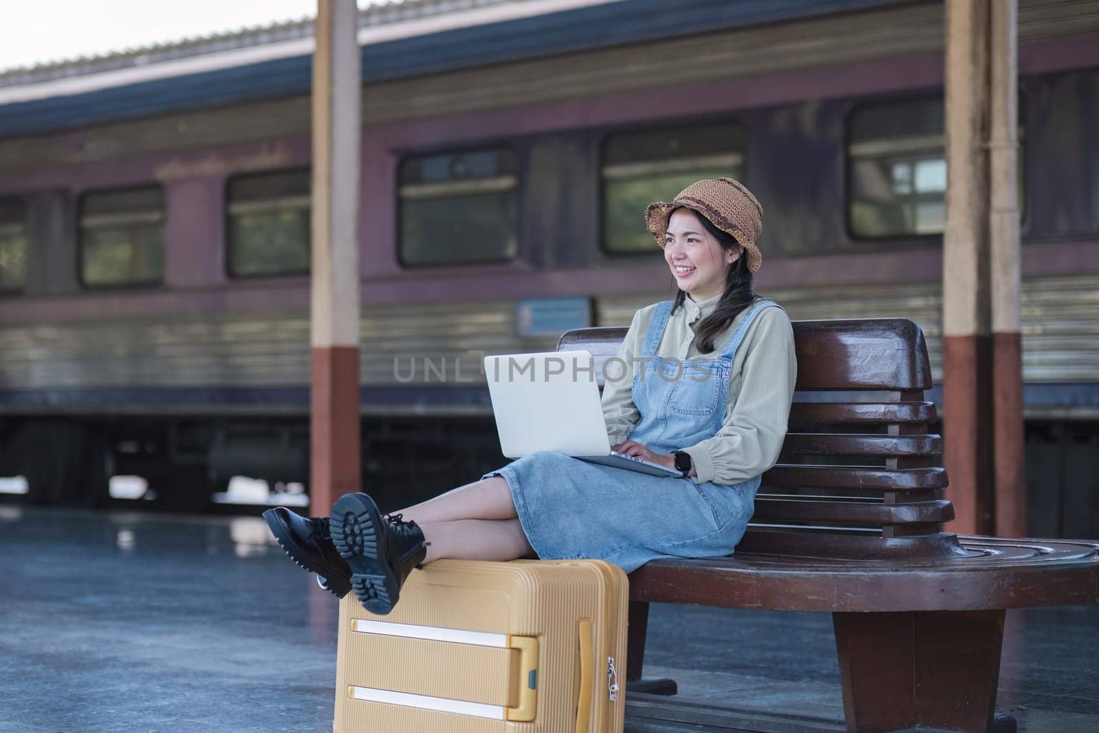 Young Asian woman in modern train station Female backpacker passenger sitting on a bench using a laptop