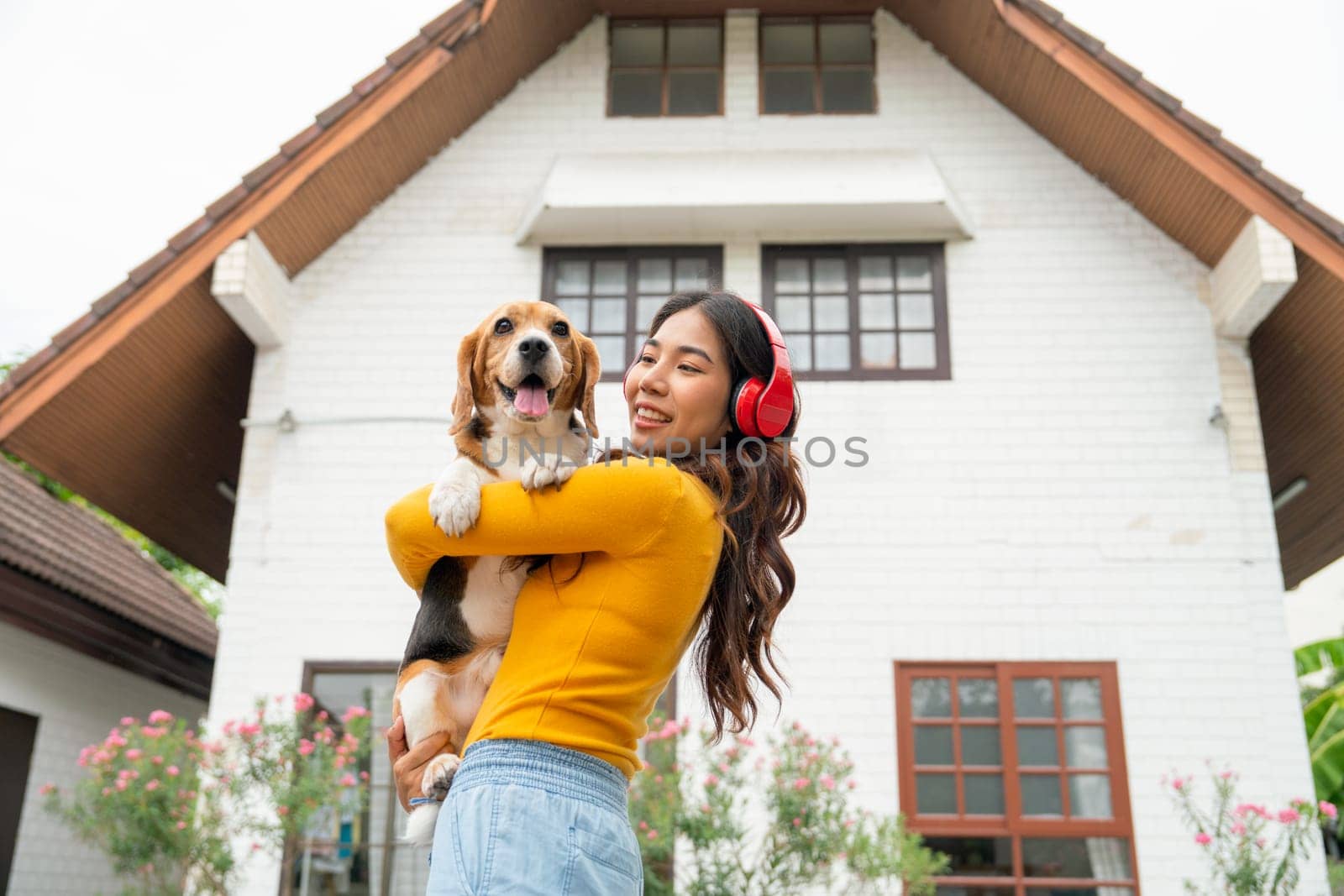 Young Asian girl with red earphone hold and hug beagle dog and stand in front of her house and she look happy with her pet.