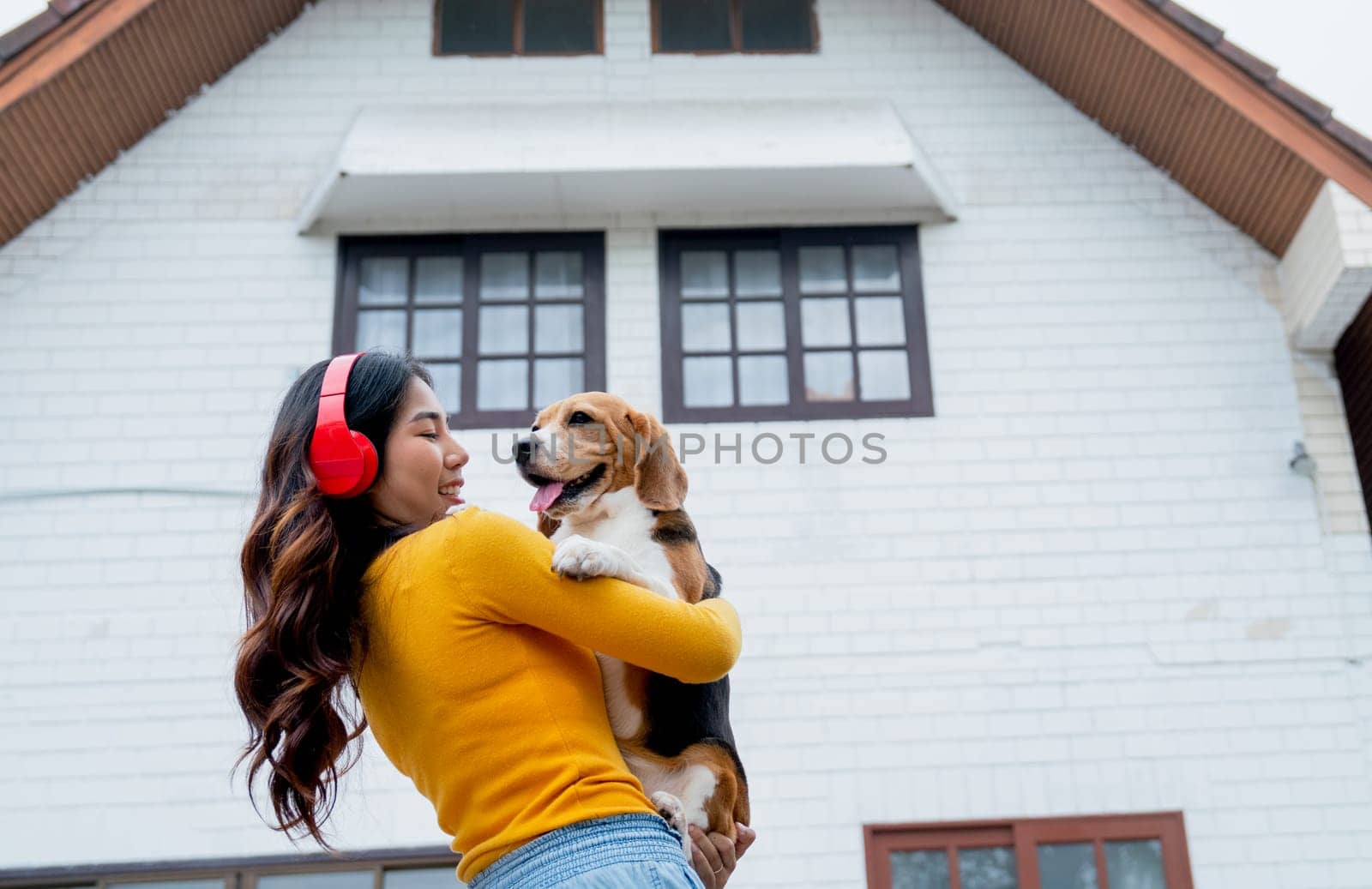 Young Asian girl with red earphone hold and hug beagle dog and stand in front of her house and she look happy with her pet.