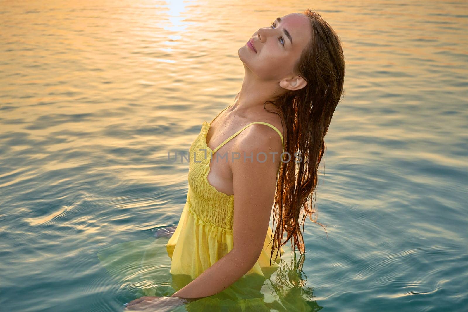 Close-up portrait of a young woman in a yellow dress at sunrise against the background of the sea. Woman walks on the seashore