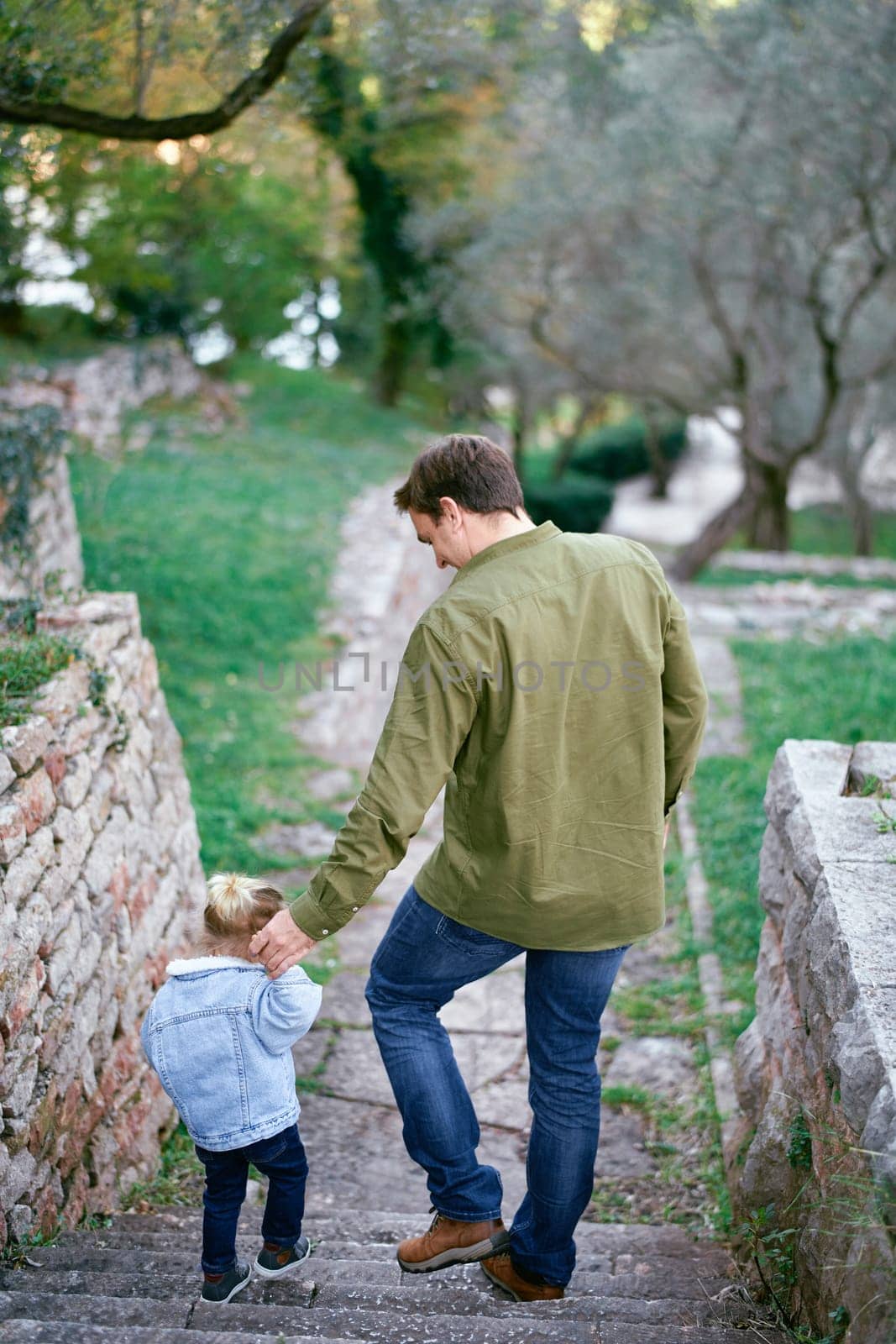 Dad and a little girl go down the stone steps, holding hands. Back view. High quality photo