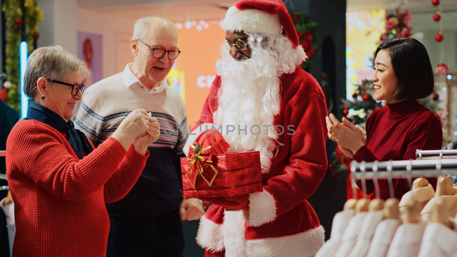 Close up shot of man dressed as Santa Claus picking raffle ticket in Christmas decorated fashion boutique during festive holiday season. Lucky senior clients winning clothing store contest