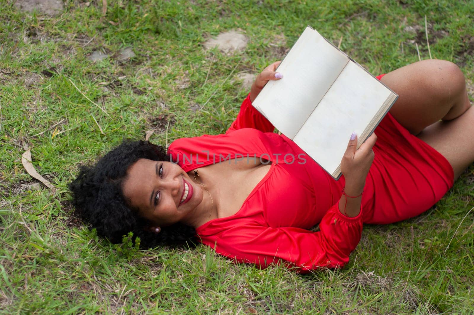 ecuadorian woman with black curly hair lying on the mountain in a red dress with an open book without text. book day. High quality photo