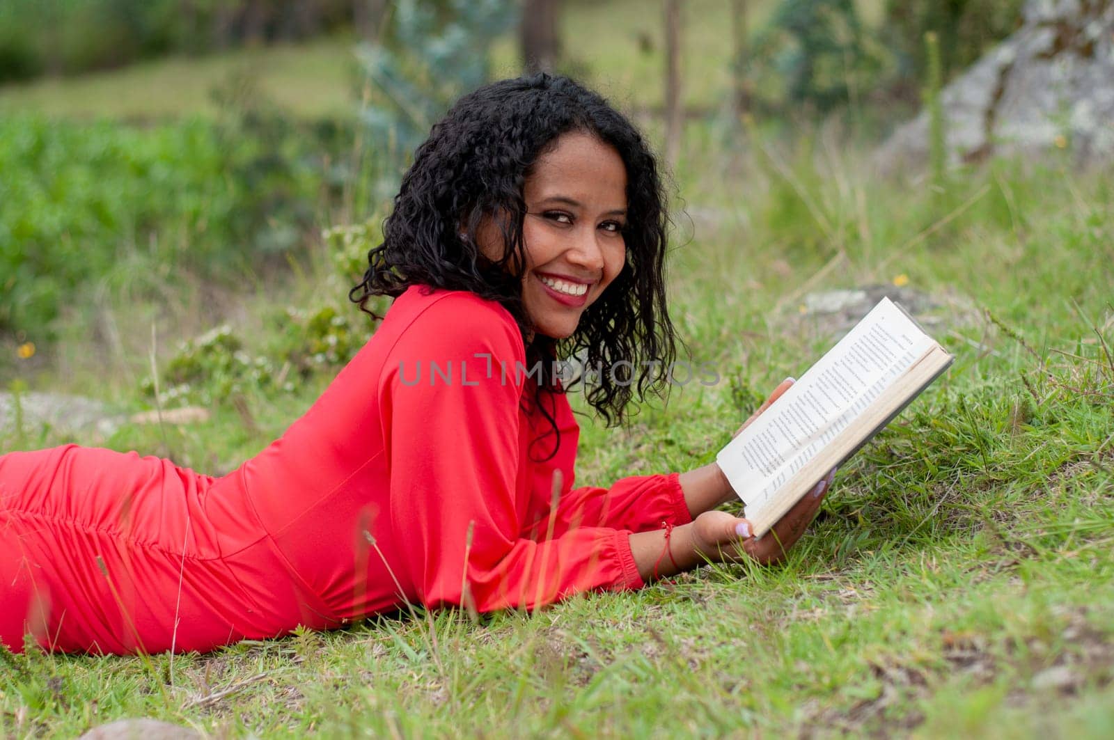 young colombian girl lying face down smiling intensely to the camera while holding a book in her hands . book day. High quality photo