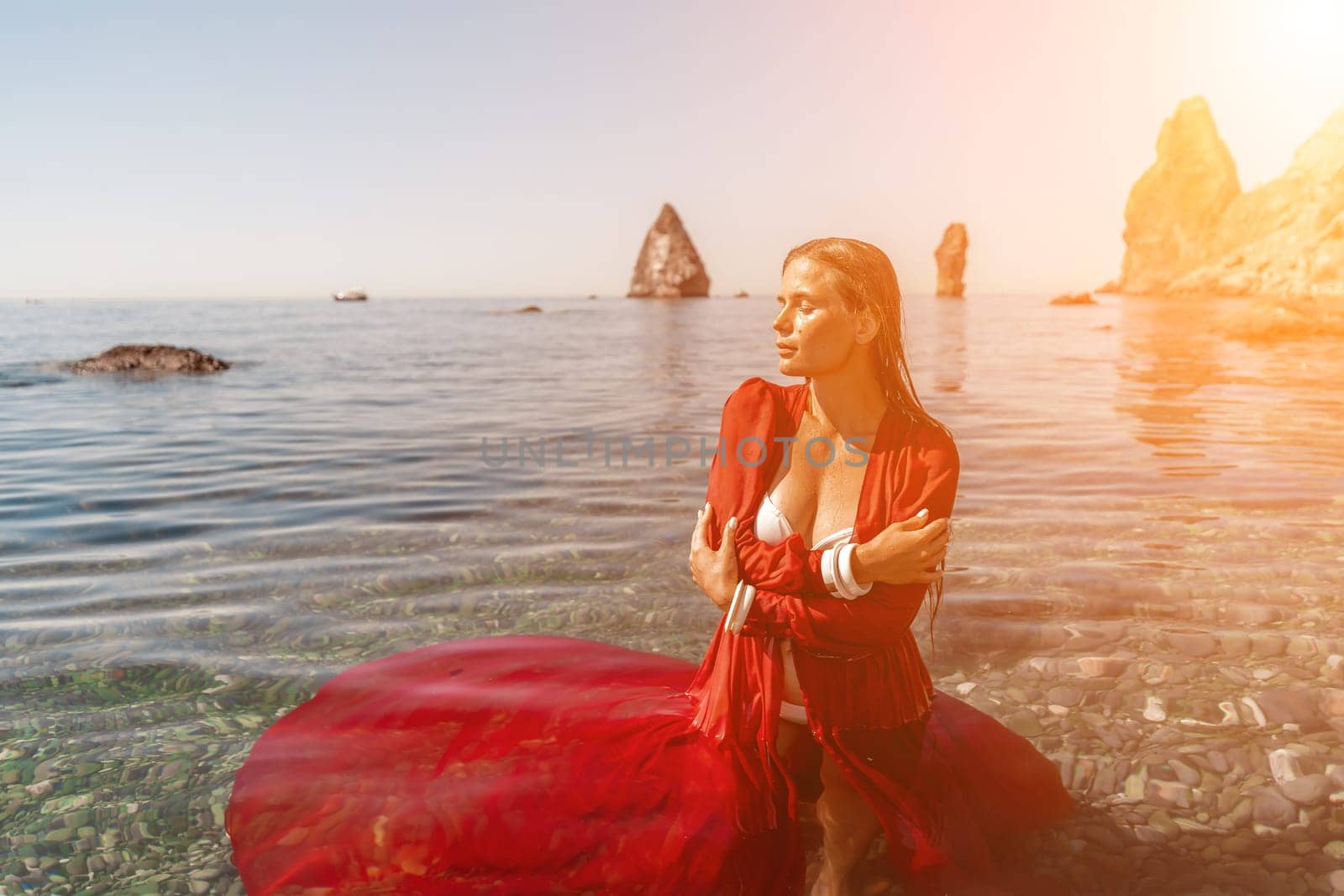 woman sea red dress. Beautiful sensual woman in a flying red dress and long hair, standing in sea in a large bay. by Matiunina