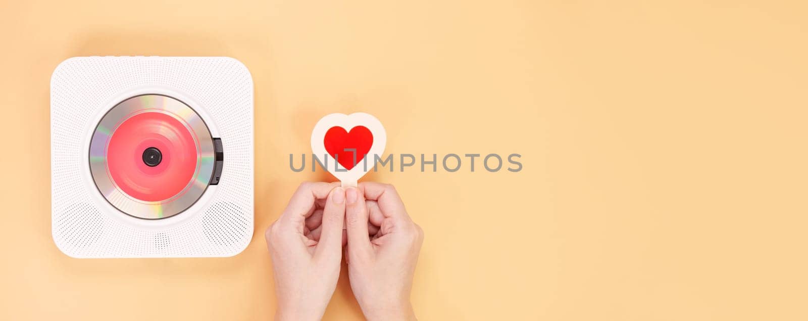 Hands holding heart shape red gift card next to white cd player with red disc on yellow background. Love music, Valentine day, Greeting, retro Love song, space for text