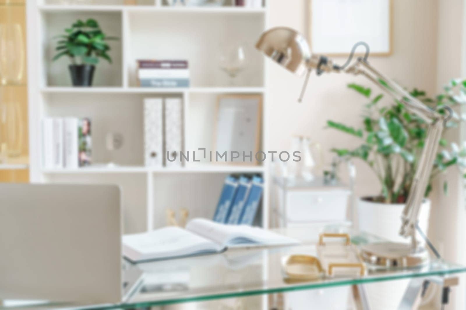Defocused blured abstract background. Comfortable workplace with a laptop in the office, at home. Bright room with large windows, bookcase, green plant. Remote work, freelance