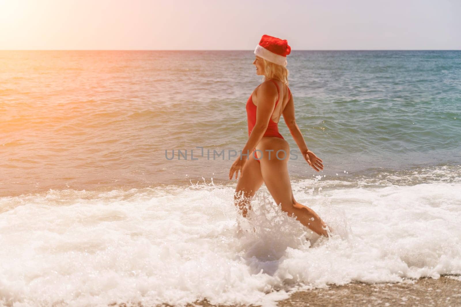 A woman in Santa hat on the seashore, dressed in a red swimsuit. New Year's celebration in a hot country by Matiunina