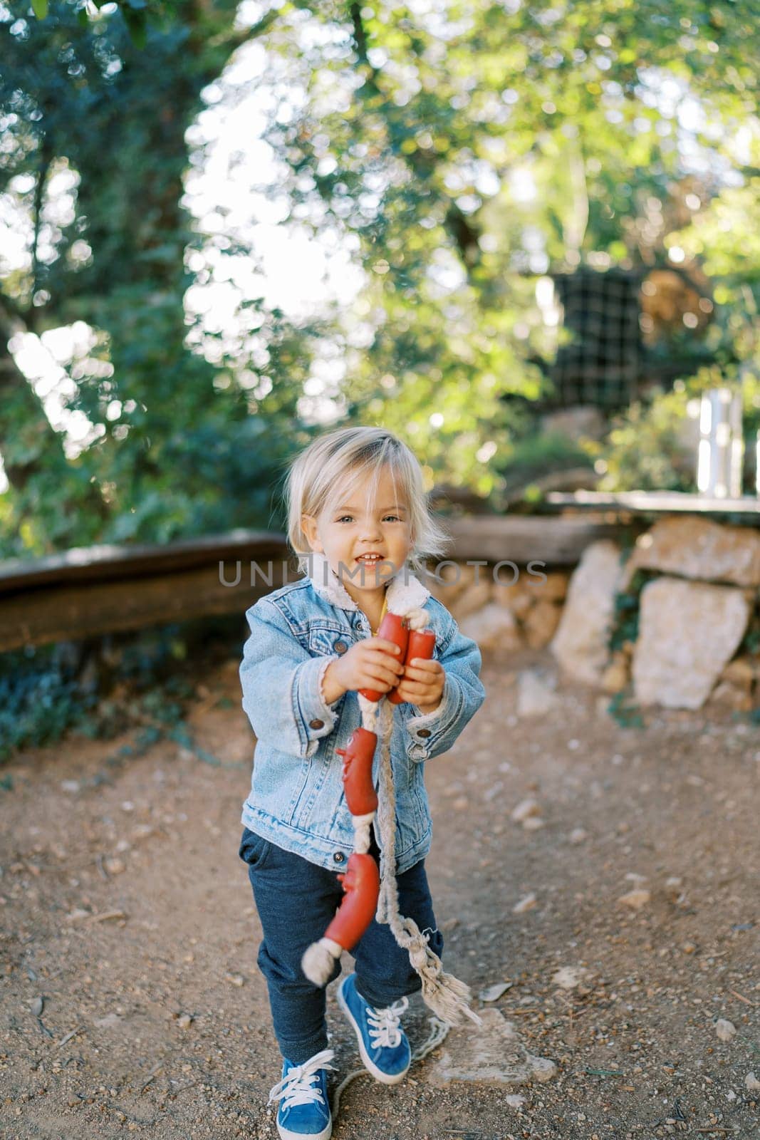 Little smiling girl stands in the park with a toy sausages on a string for dogs in her hands. High quality photo