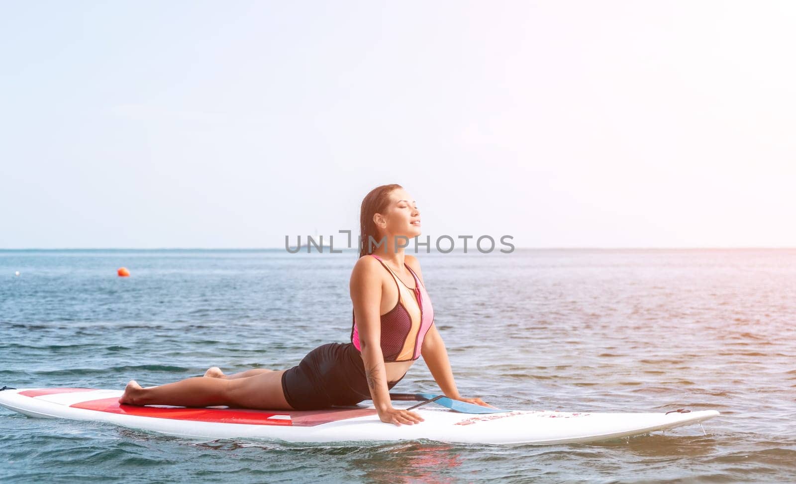 Woman sup yoga. Happy young sporty woman practising yoga pilates on paddle sup surfboard. Female stretching doing workout on sea water. Modern individual female outdoor summer sport activity