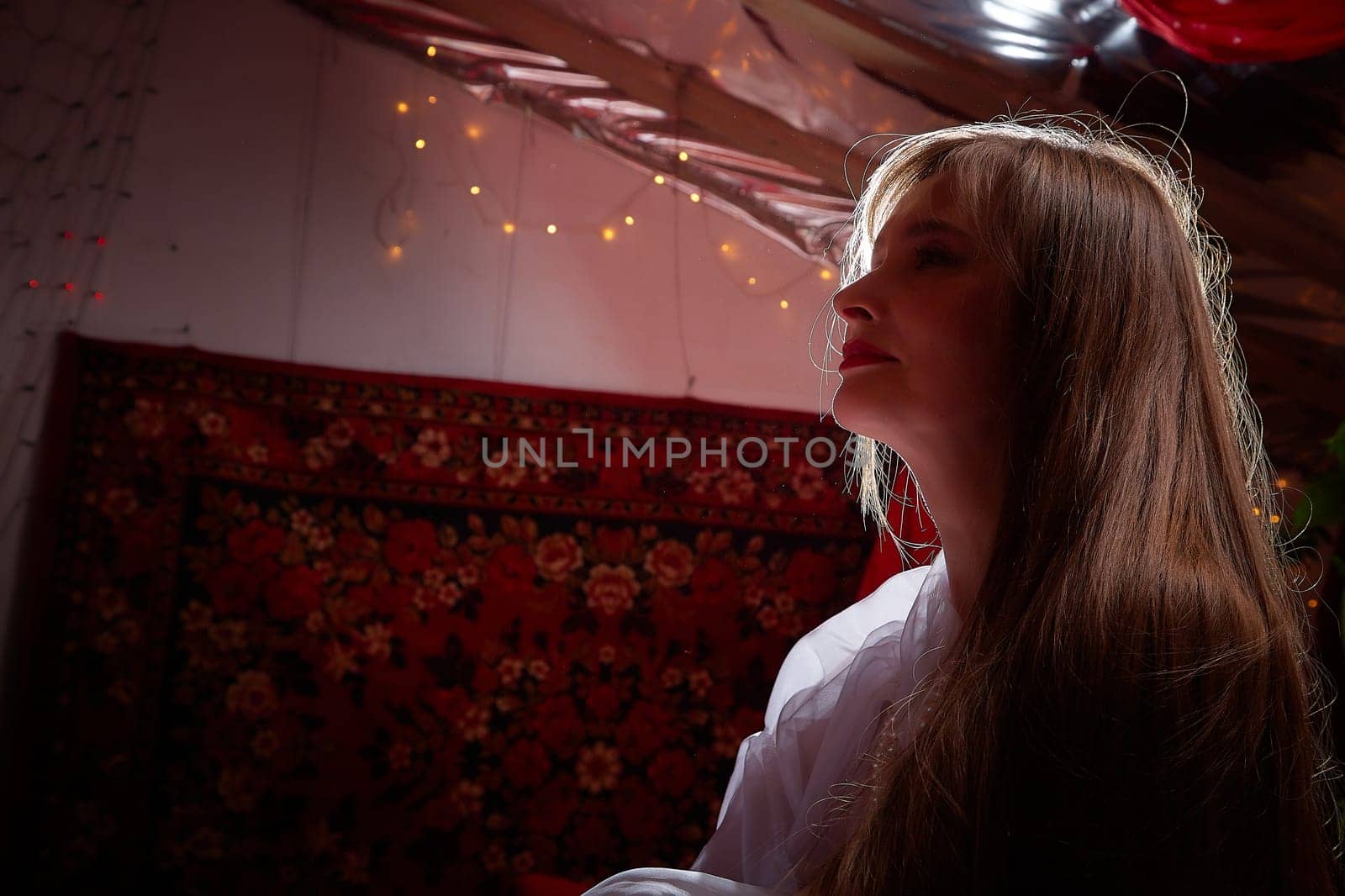 Beautiful European girl looking like Arab woman in red room with rich fabrics and carpets in sultan harem. Photo shoot of an oriental style odalisque. A model poses in sari as indian woman in india