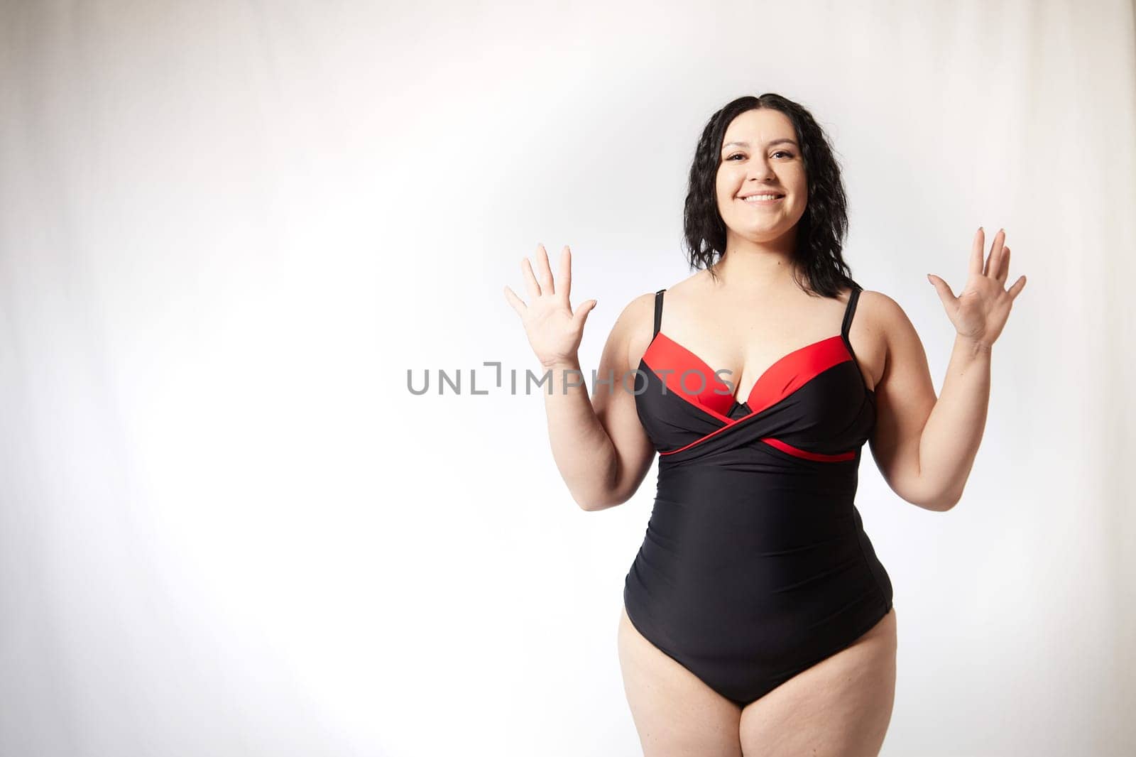 Portrait of attractive dreamy thick woman in red black swimsuit posing on white background. Body positive, photoshoot, selfie. Funny plus size model