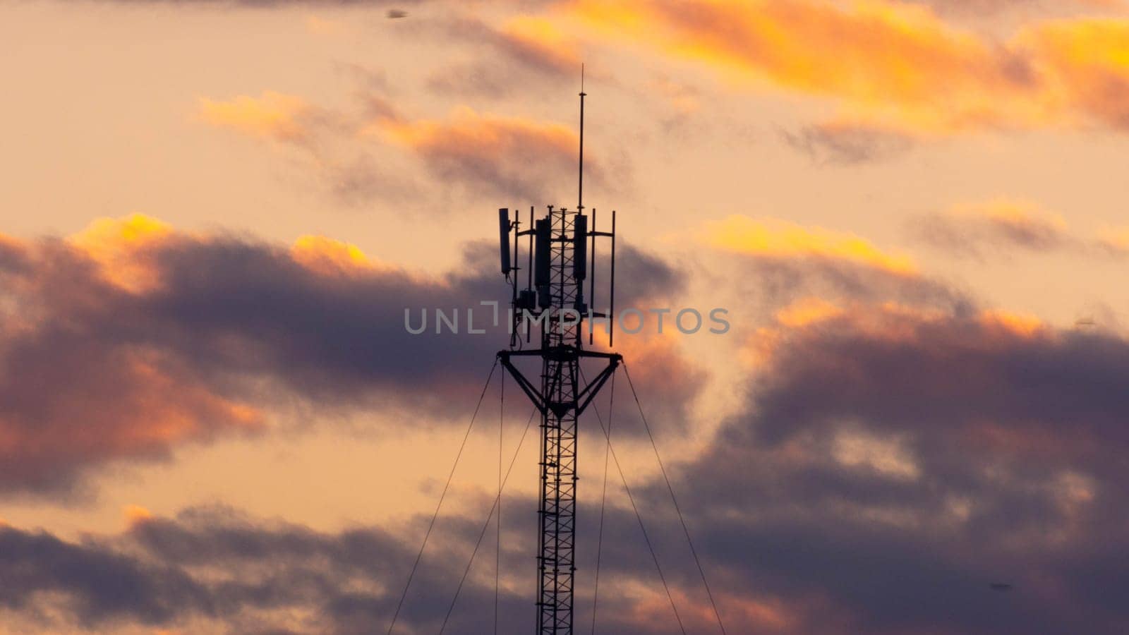 Telecommunications tower with beautiful sky at sunrise. Electronic antenna with clouds and orange sky background. Modern business communication by TEERASAK