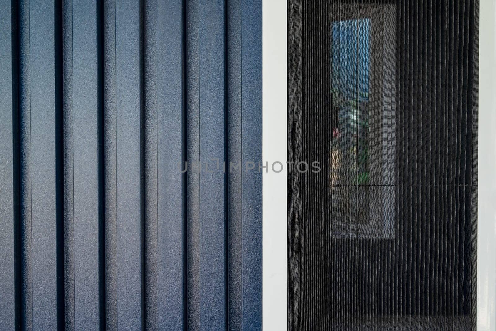 House with a facade covered with dark blue PVC panels and fly screen applied to the windows