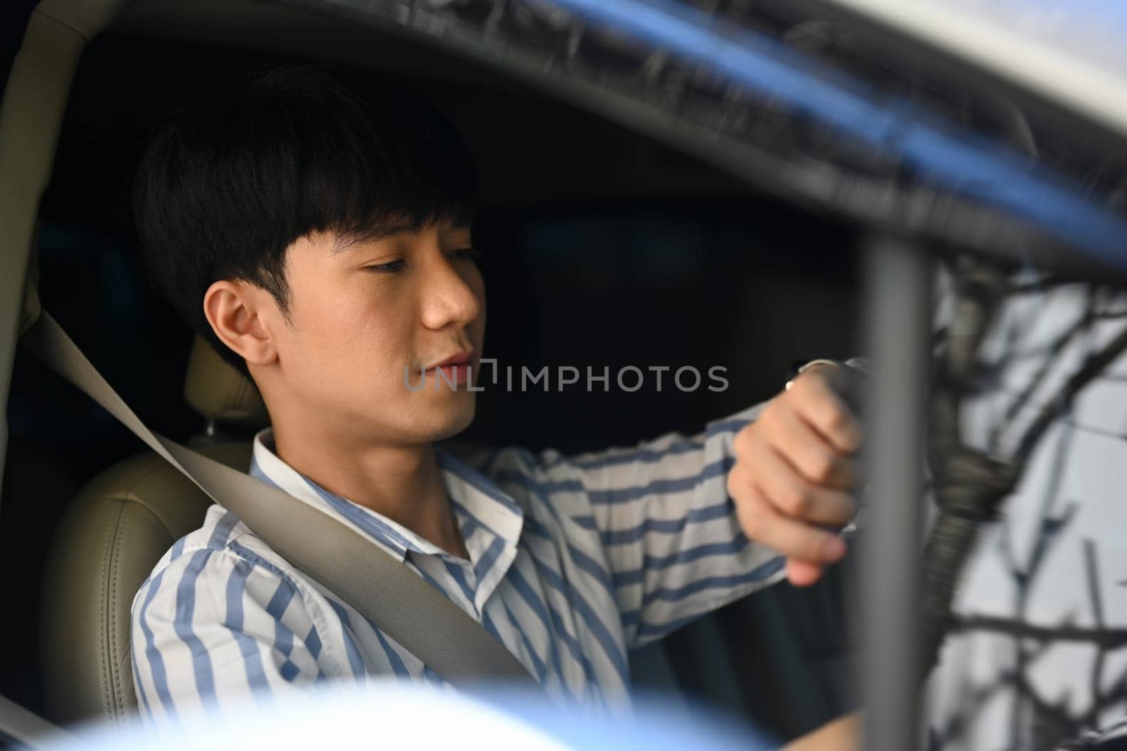 Young businessman checking time on wrist watch while driving to the office. by prathanchorruangsak