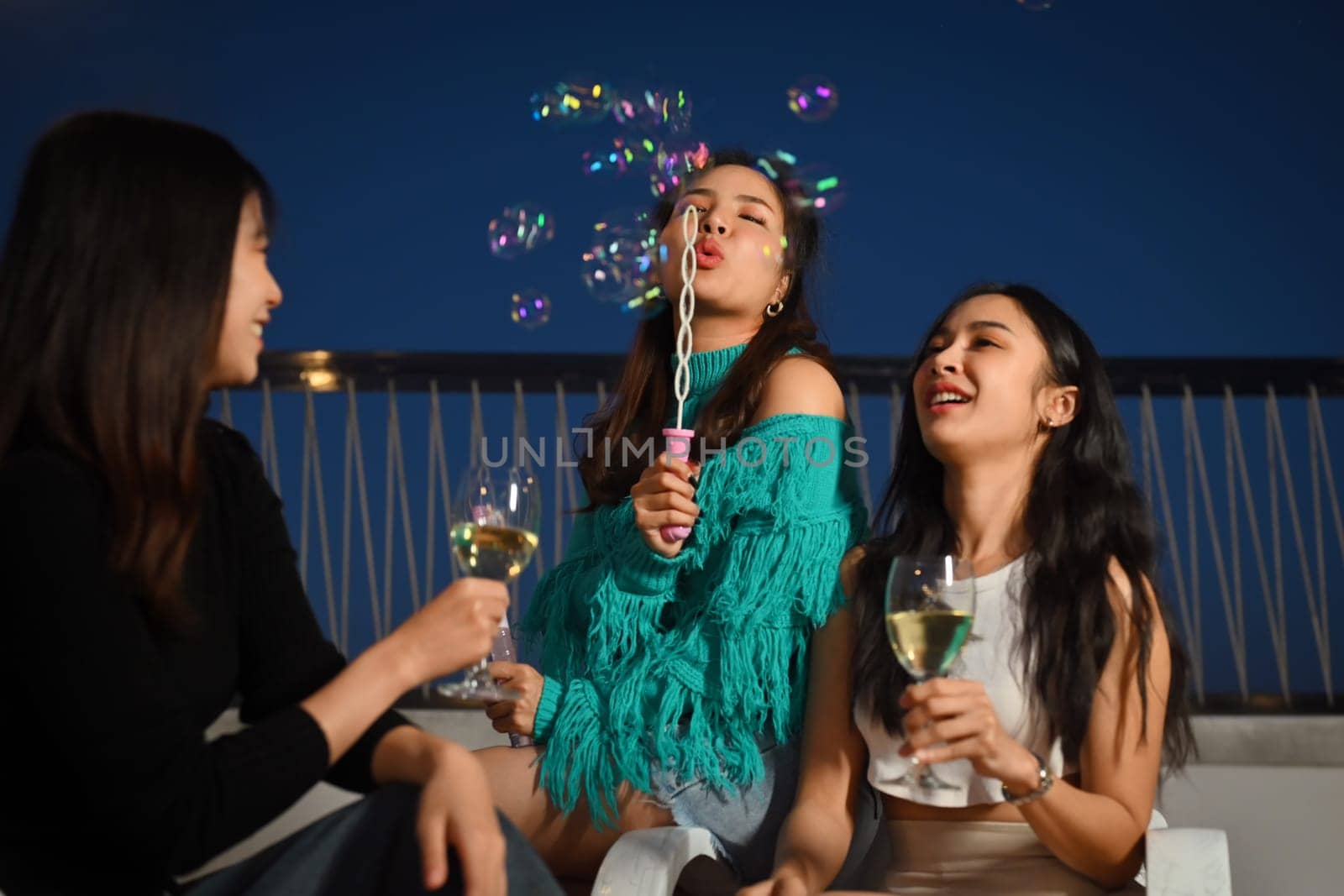 Group of young people having fun at outdoor rooftop party with drinks and blowing soap bubbles