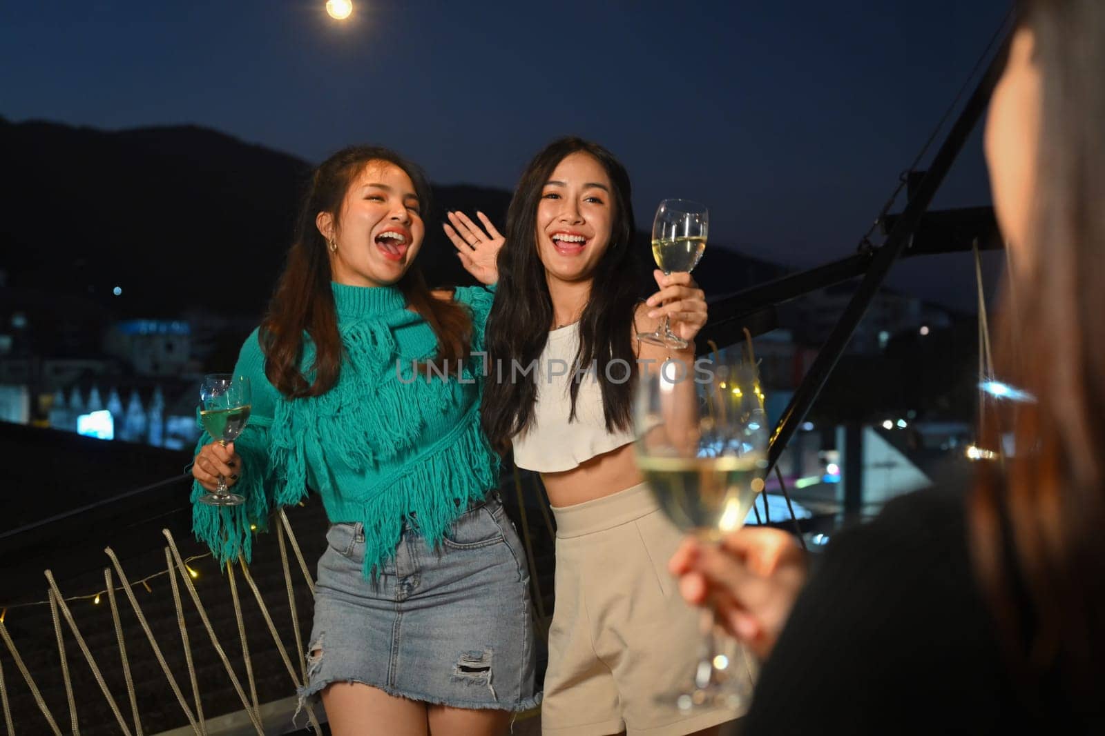 Cheerful female friends feeling excited meeting friend in rooftop party. Holidays, party, celebration and people concept