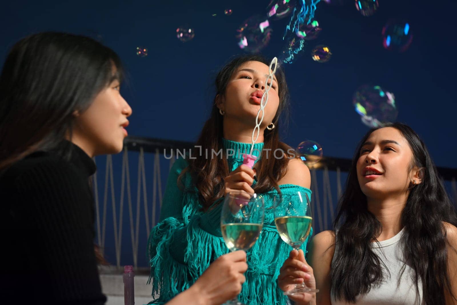 Happy friends having fun enjoy chill with drinks and blowing soap bubbles at outdoor rooftop party