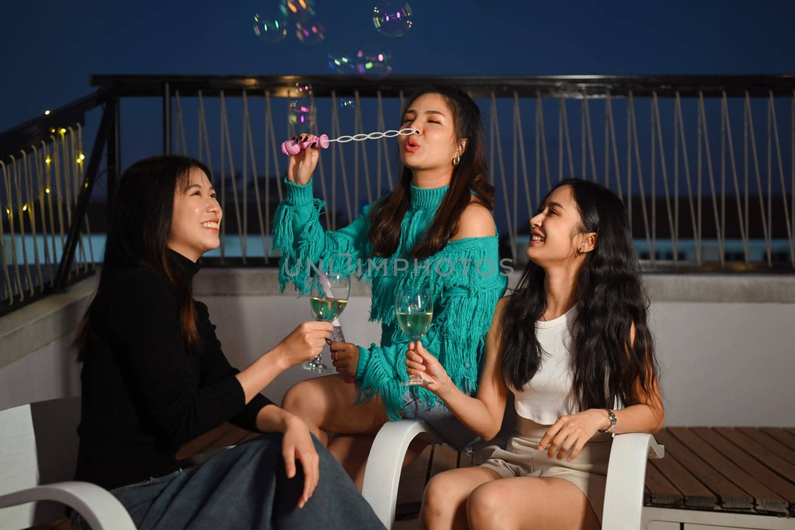 Young friends gathered together having fun toasting champagne and blowing soap bubbles at the rooftop night party