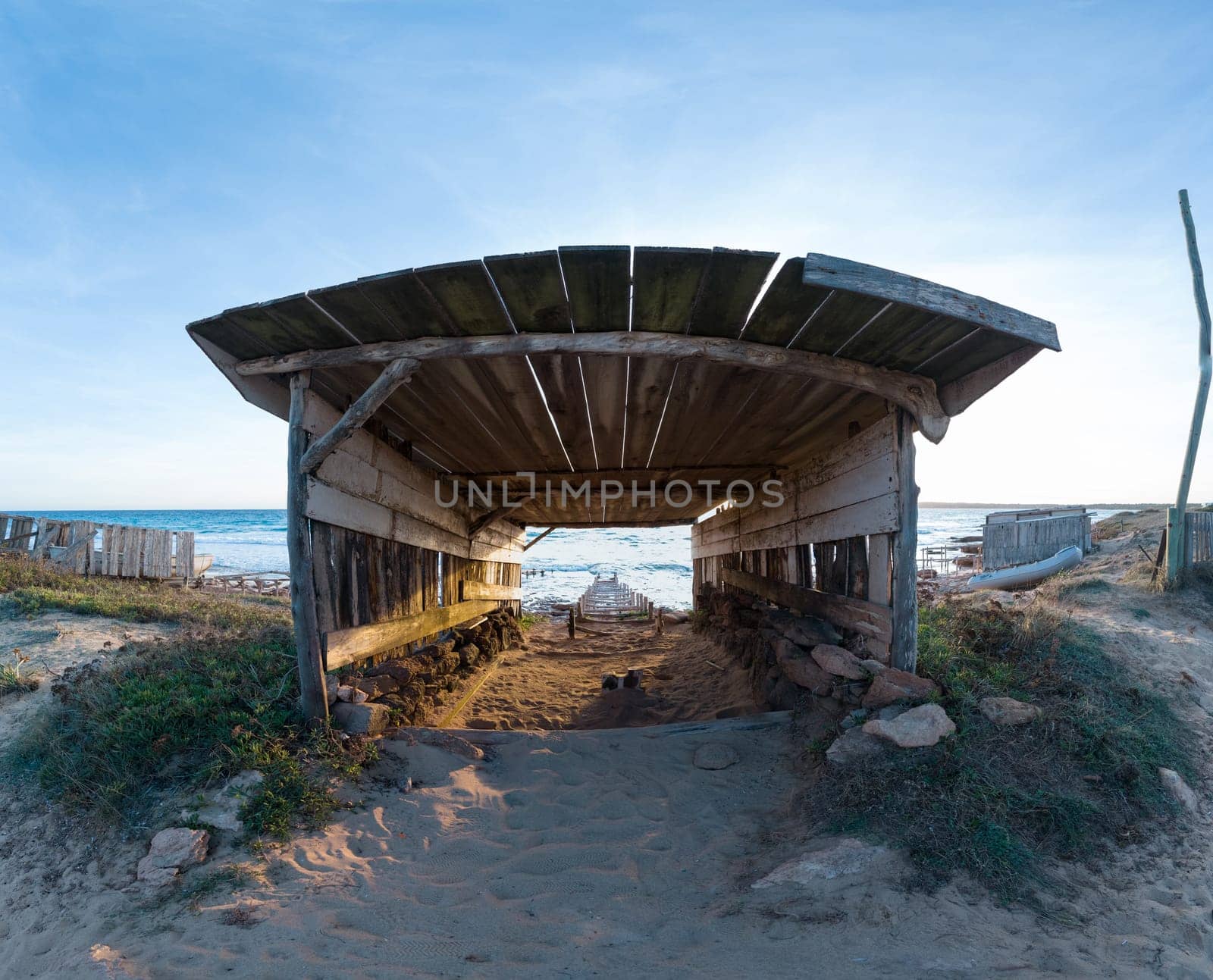 A picturesque scene of an old boat shed with a track to the sea at sunset.