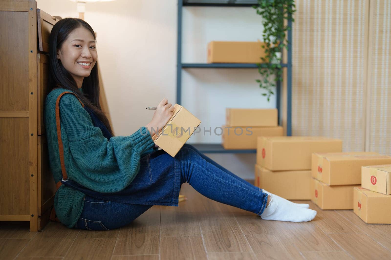 Starting small business entrepreneur of independent young Asian woman online seller is using computer and taking orders to pack products for delivery to customers. SME delivery concept by Manastrong