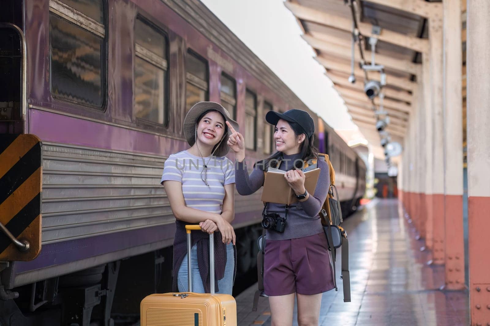 Two Asian female tourist friends are at the train station. Waiting for the train to travel to the provinces together on the weekend..