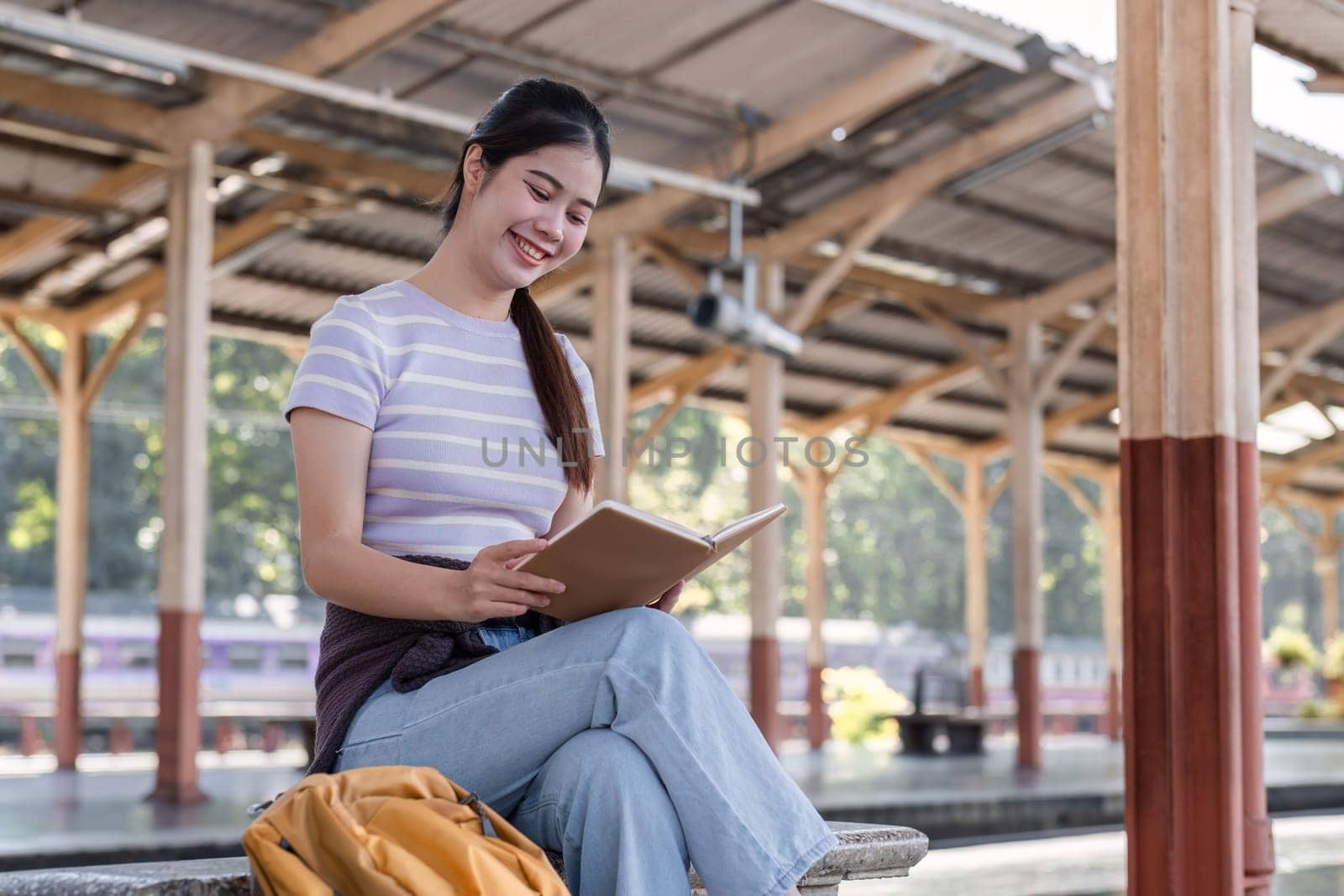 Young Asian woman in modern train station Female backpacker sitting on a bench reading a book while waiting for a train