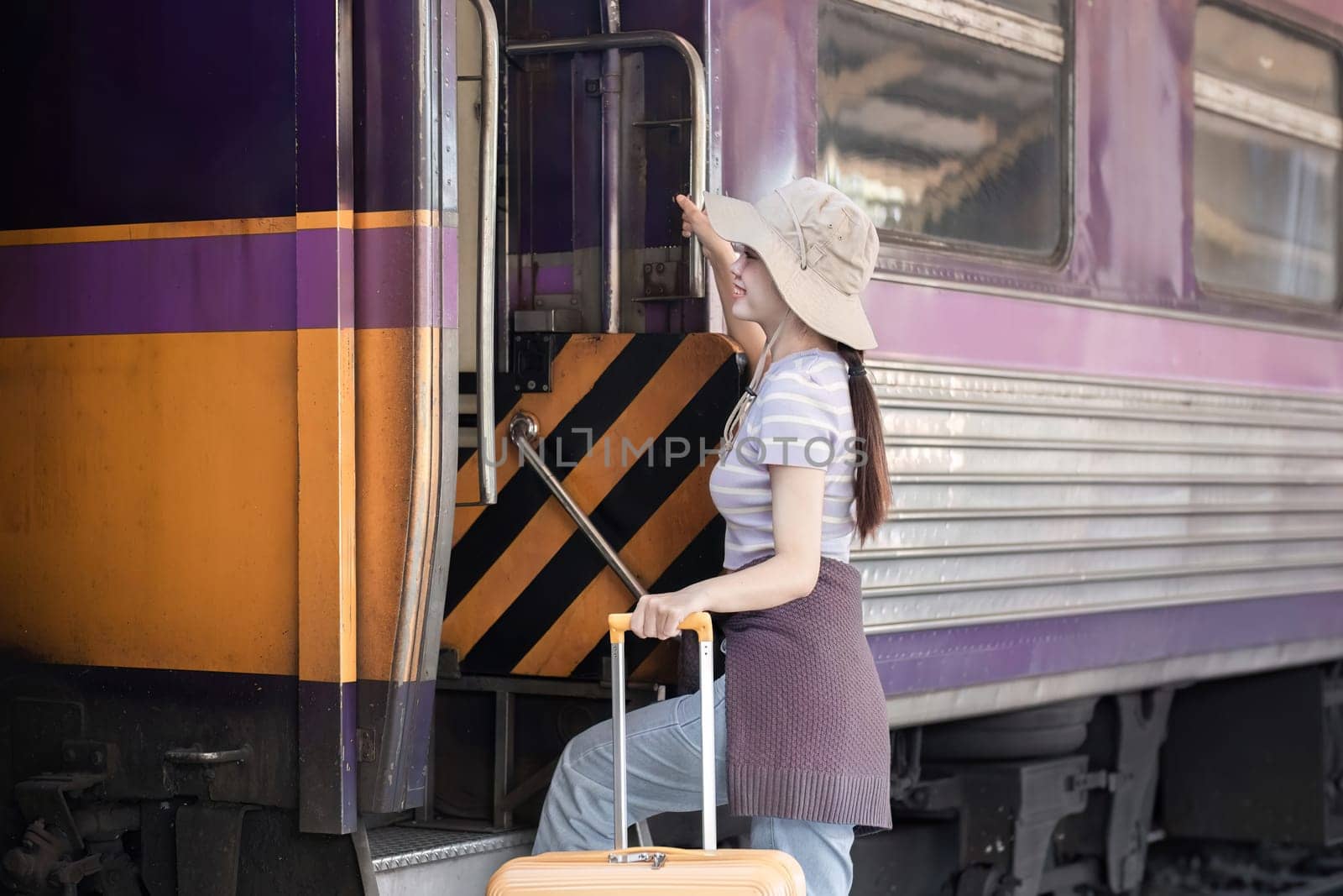 Young woman wearing an explorer's hat and carrying a suitcase Stand and look for a train at the train station. Traveler's concept by wichayada