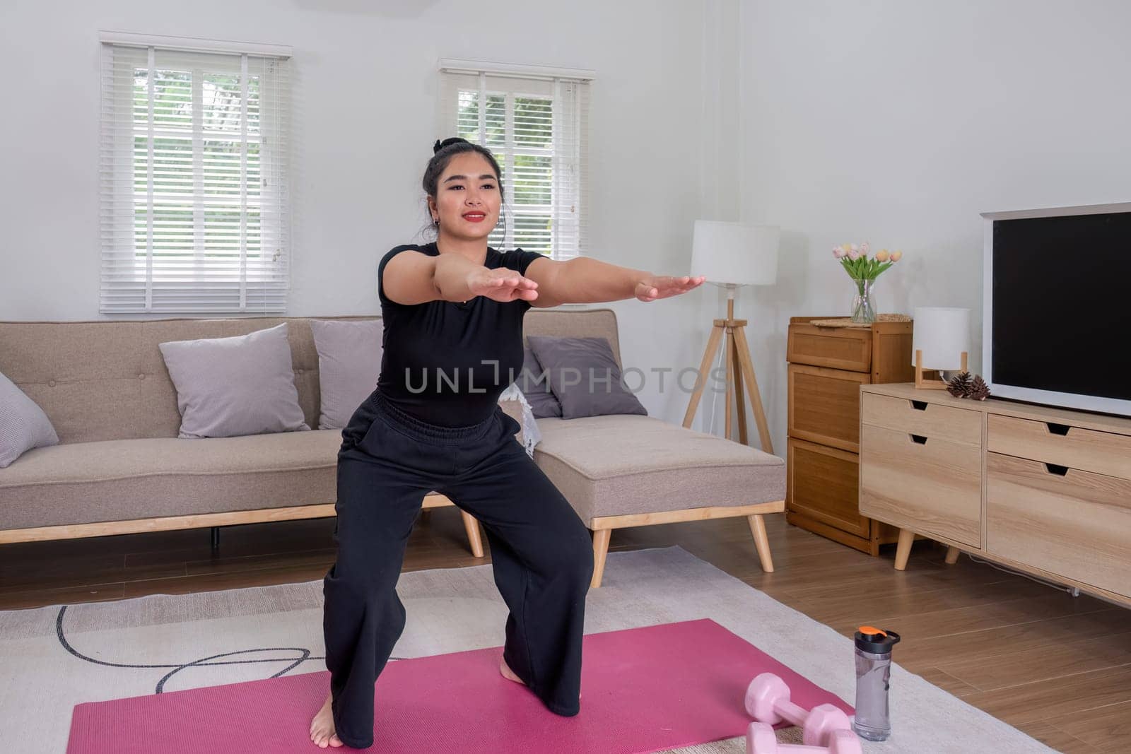 Fat woman exercising at home A beautiful oversized woman in a sports bra and casual pants stands in the living room and exercises..