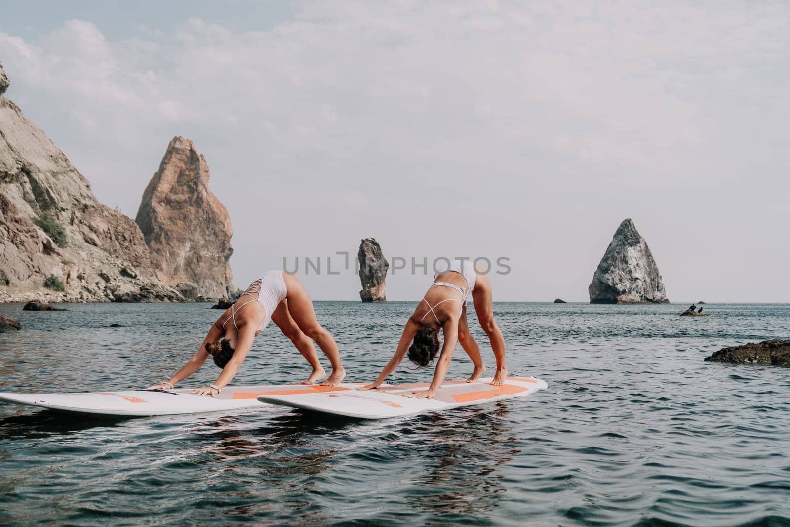 Woman sup yoga. Happy sporty woman practising yoga pilates on paddle sup surfboard. Female stretching doing workout on sea water. Modern individual female hipster outdoor summer sport activity. by panophotograph