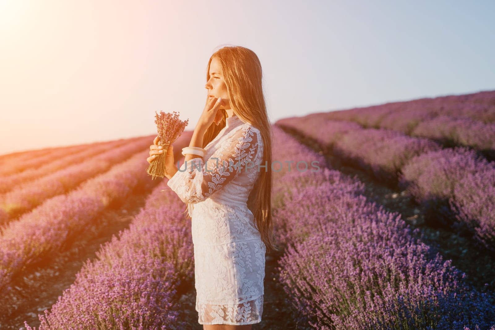 Woman lavender field. Happy carefree woman in a white dress walking in a lavender field and smelling a lavender bouquet on sunset. Ideal for warm and inspirational concepts in wanderlust and travel. by panophotograph