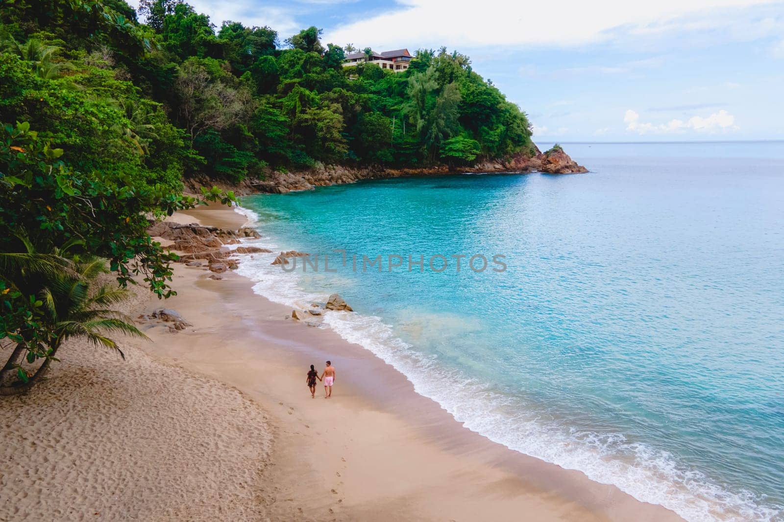 A couple of men and women relaxing on a white tropical beach with palm trees in Phuket Thailand by fokkebok