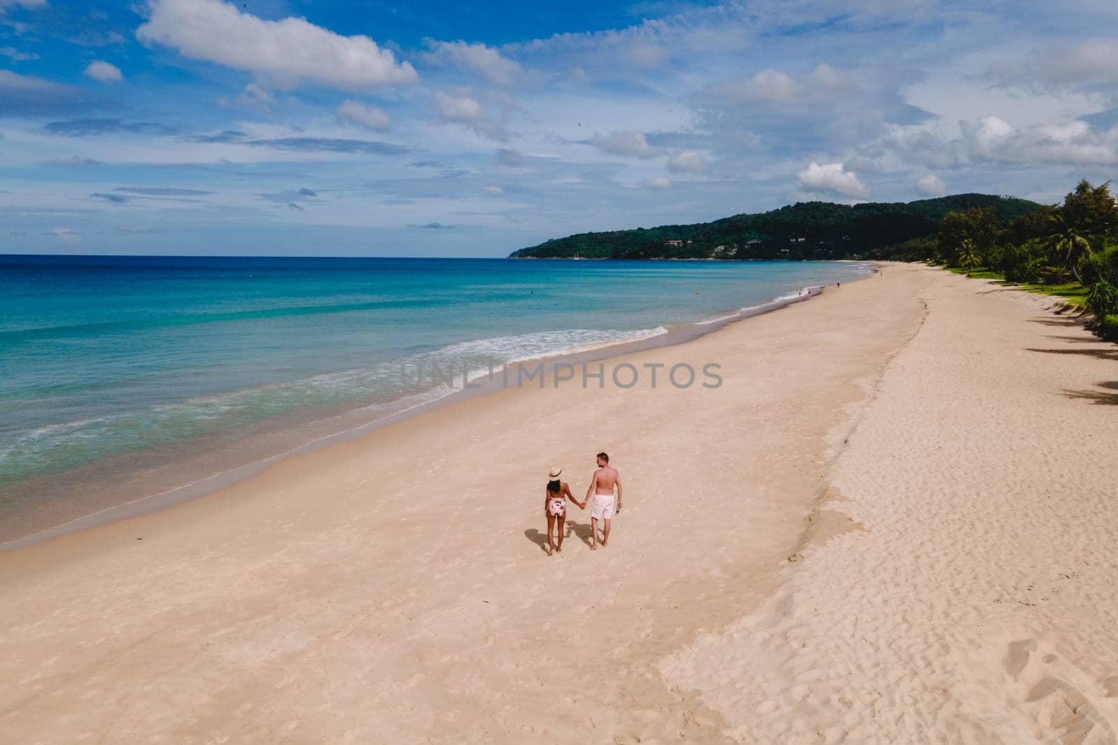 A couple of men and women are relaxing on a white tropical beach with palm trees in Phuket Thailand. Karon Beach Phuket on a sunny day