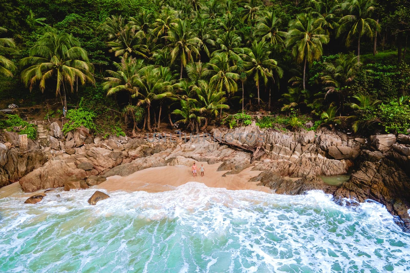 A couple of men and women relaxing on a white tropical beach with palm trees in Phuket Thailand by fokkebok