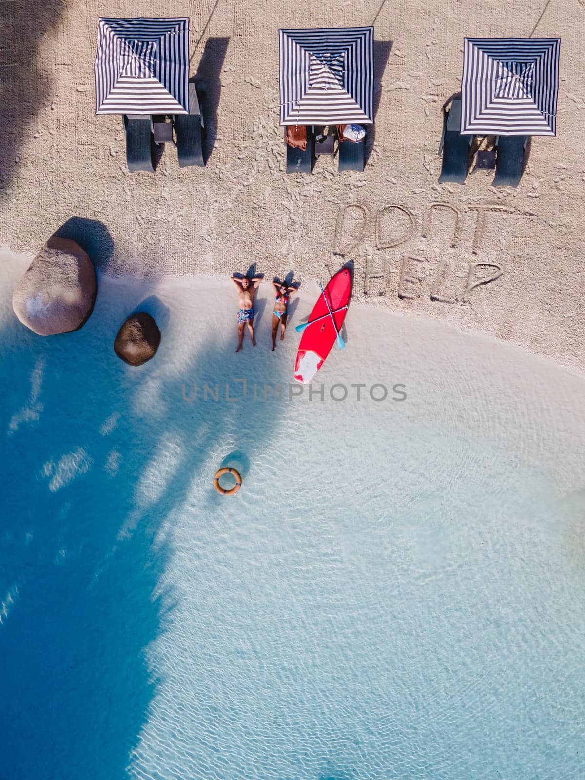 A couple of men and women are relaxing on a white tropical beach with beach chairs in Phuket Thailand. Dont help sign on a white beach drone top view