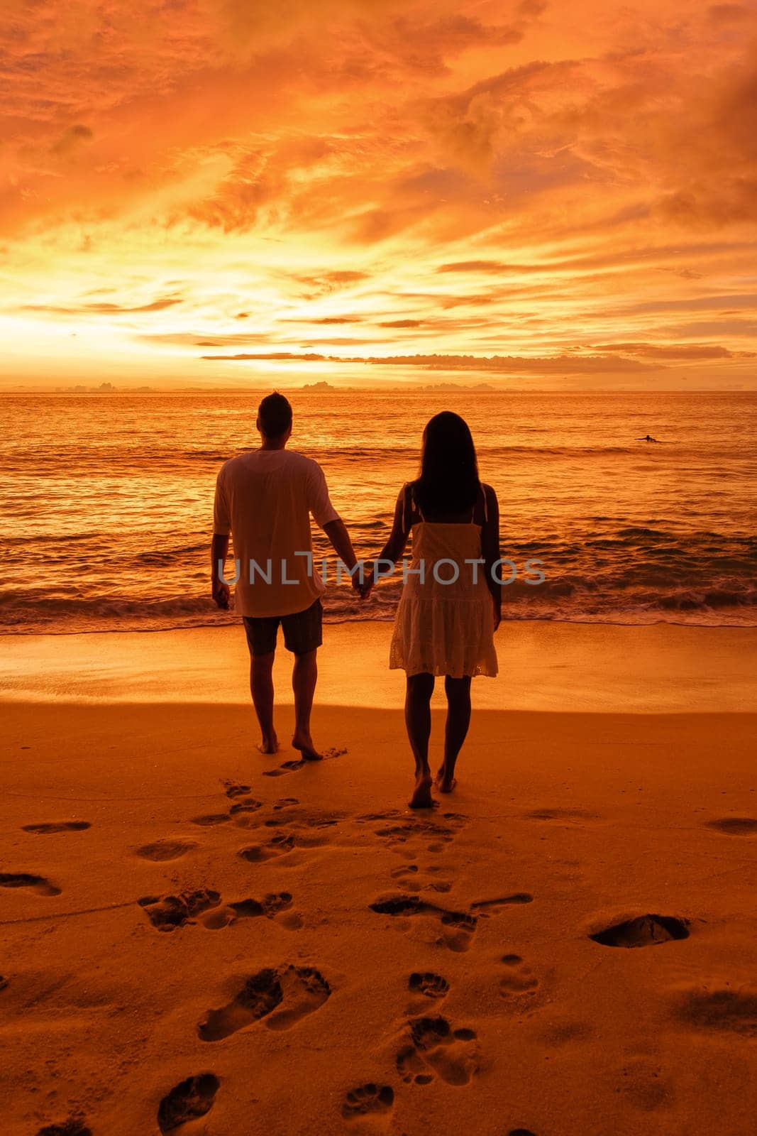 A couple of men and woman watching sunset at Naithon Beach Phuket Thailand, a famous surf spot in Phuket, Naithon beach at sunset.