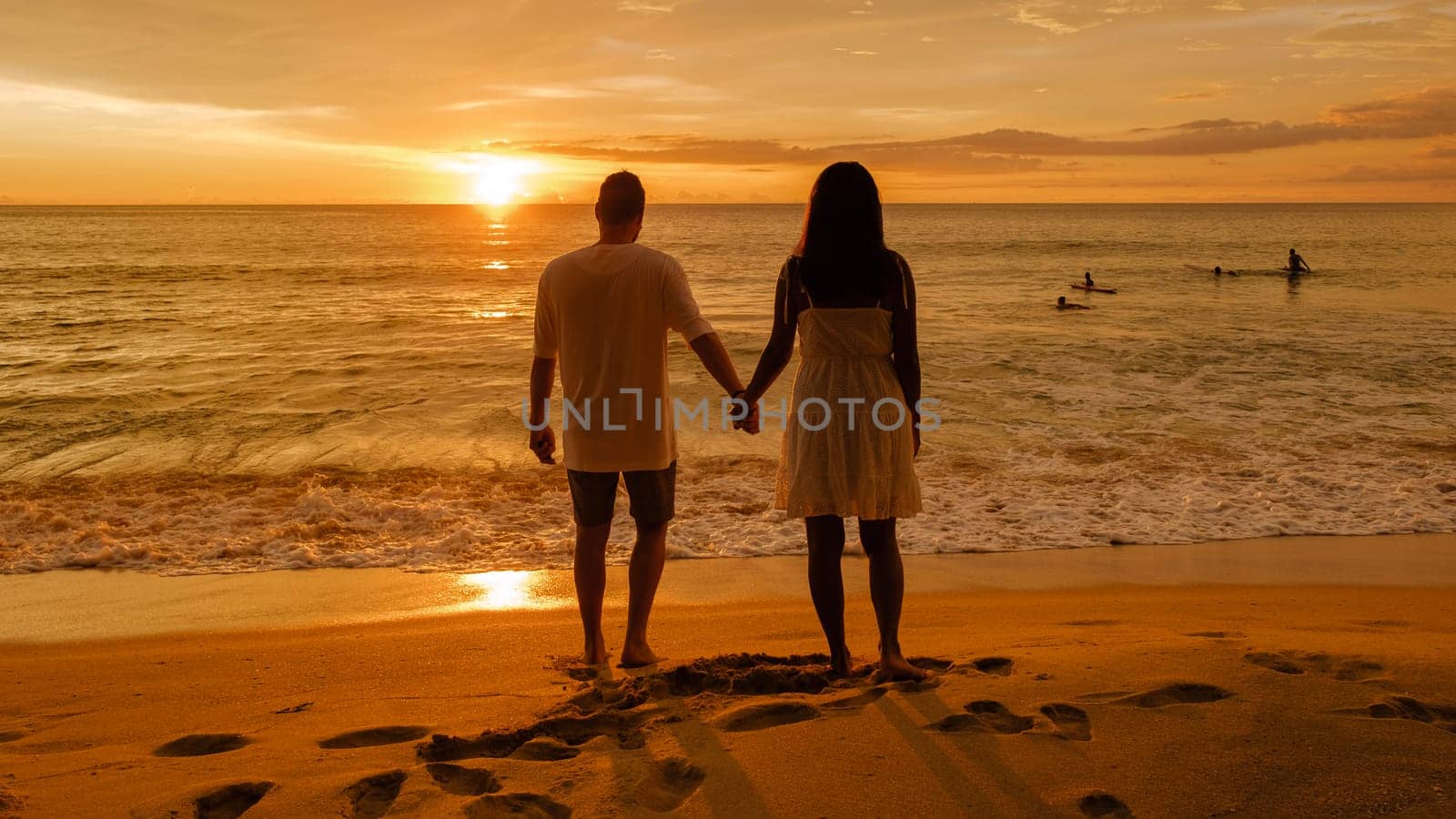 A couple of men and woman watching sunset at Naithon Beach Phuket Thailand, a famous surf spot in Phuket, Naithon beach at sunset.