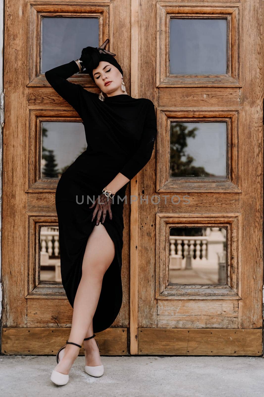 Stylish woman in the city. Fashion photo of a beautiful model in an elegant black dress posing against the backdrop of a building on a city street.