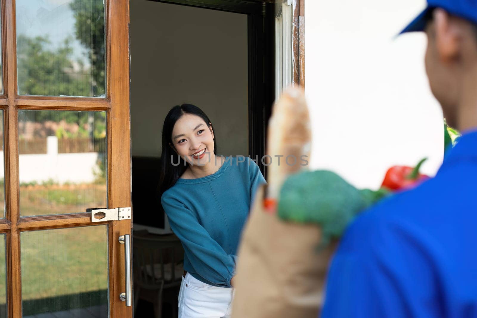 Asian deliver man worker handling bag of food, fruit, vegetable give to young beautiful female in front of the house by itchaznong